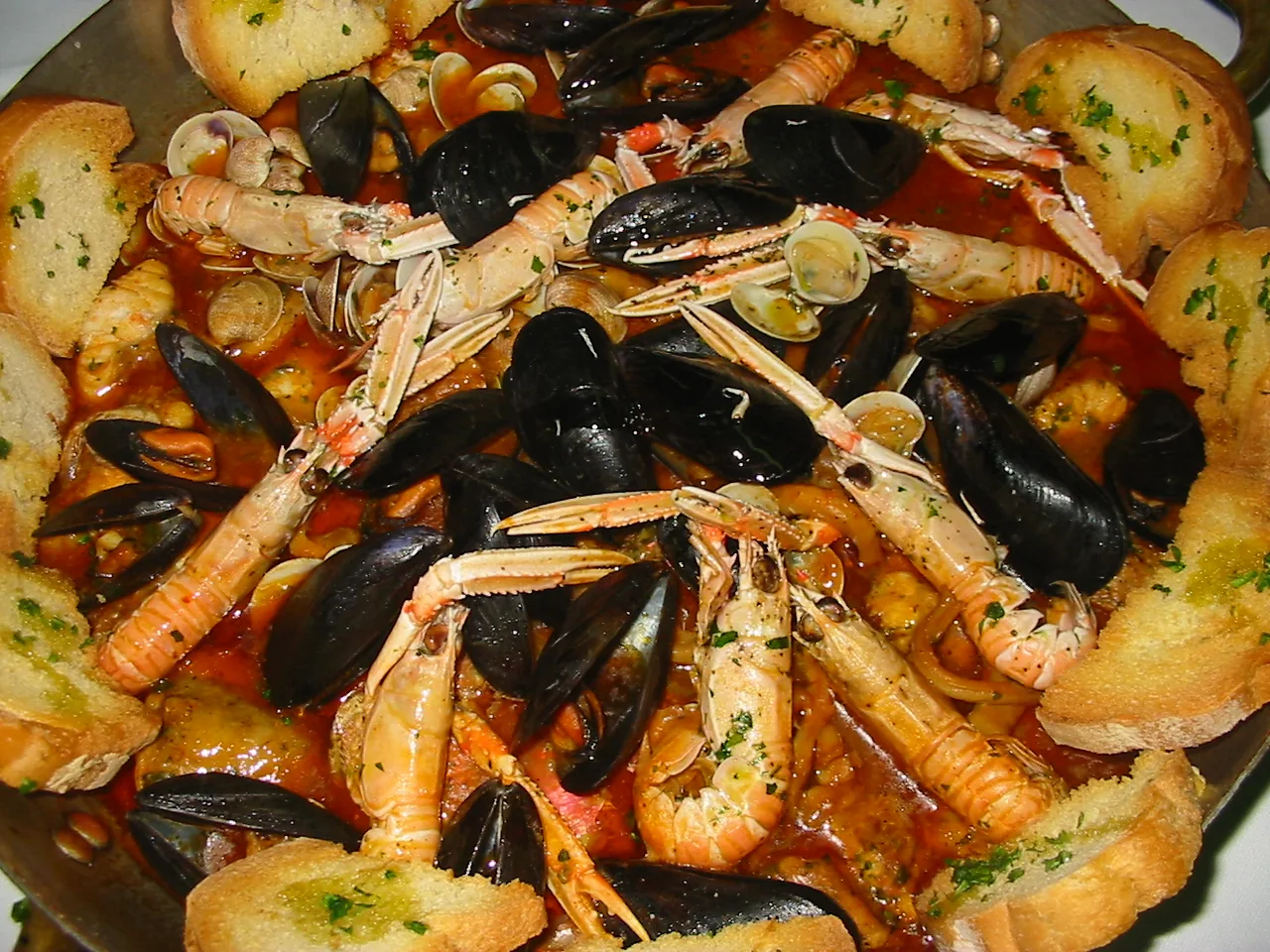 Un piatto di brodetto di pesce con cozze, scampi e crostini